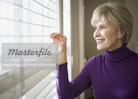 Mature woman looking through blinds of a window