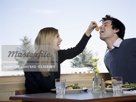 Close-up of a young woman feeding a slice of tomato to a young man