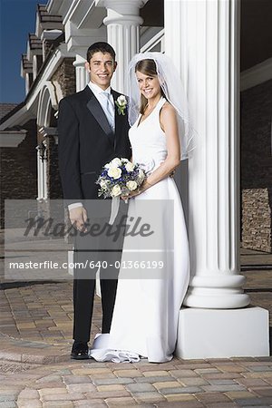 Portrait of a newlywed couple standing together and smiling near a column
