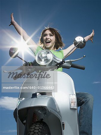 Low angle view of a teenage girl riding a scooter with her arms raised