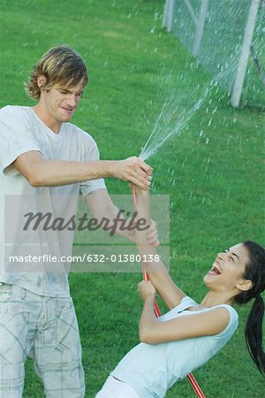 Young friends playing with garden hose, getting wet