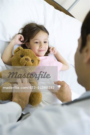 Fille couché dans son lit d'hôpital, en souriant vers le haut au médecin