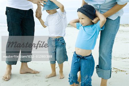 Parents putting sunhats on children at the beach, low section