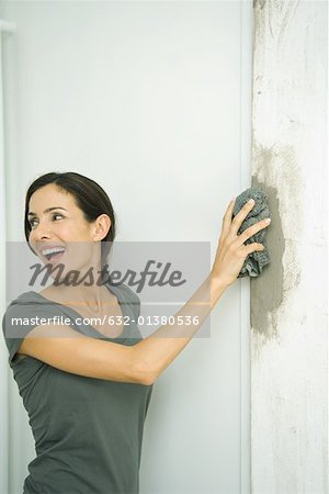 Femme essuyant le coulis sur le mur avec un chiffon humide, regarder par-dessus l'épaule
