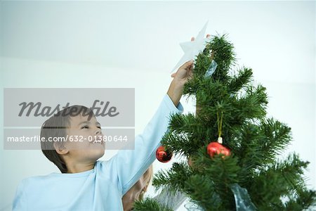 Boy putting star on top of Christmas tree