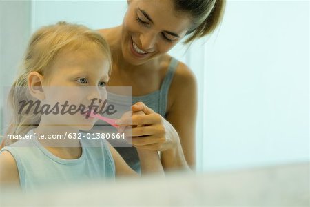 Mother and daughter brushing girl's teeth together