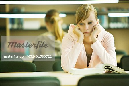 Female college student sitting at table in library, leaning on elbows