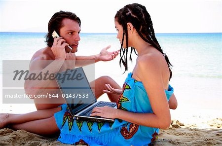 Junges Paar am Strand mit Laptop und Handy