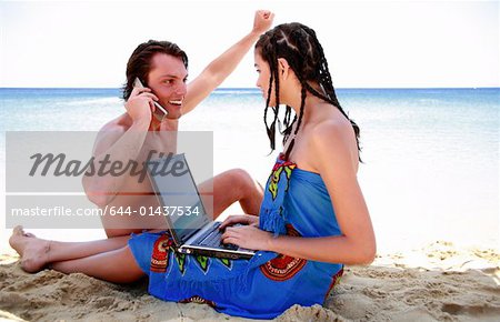 Junges Paar am Strand mit Laptop und Handy
