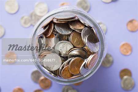 Glass jar with coins and scattered coins