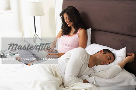 Couple in Bed, Woman Using Laptop