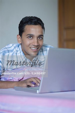 Portrait of a young man using a laptop on a bed