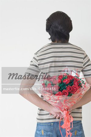 Rear view of a man holding a bouquet of flowers behind his back