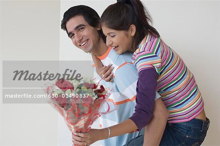 Side profile of a young woman riding piggyback on a young man and holding a bouquet of flowers