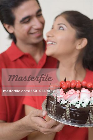 Close-up of a young couple holding a chocolate cake and looking at each other