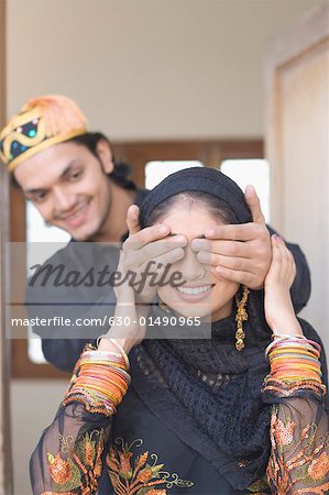 Close-up of a young man covering his wife's eyes from behind