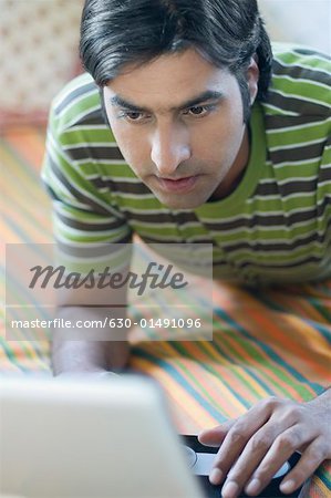 Close-up of a mid adult man lying on a bed and using a laptop