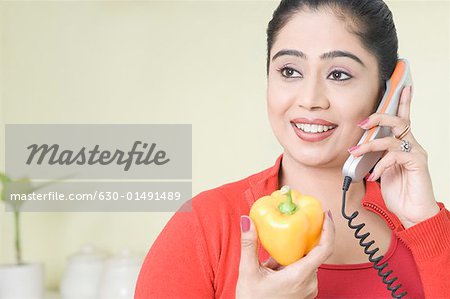 Young woman talking on the telephone and holding a yellow bell pepper