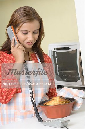 Young woman holding a cake in a mould and talking on a telephone