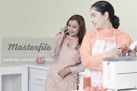 Young woman using an electric mixer with another woman talking on a mobile phone