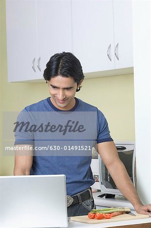 Young man standing in a kitchen and using a laptop