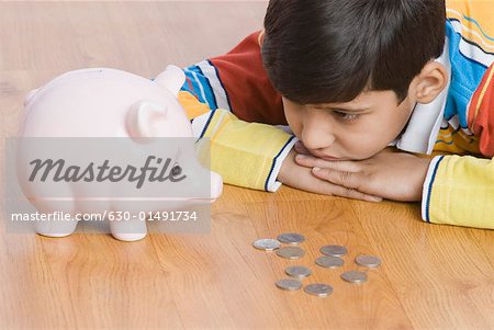 Close-up of a boy lying in front of a piggy bank