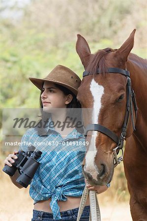 Teenage girl standing with a horse and holding a pair of binoculars