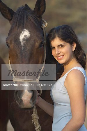 Portrait d'une jeune adolescente debout avec un cheval et souriant