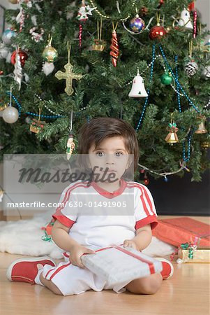 Portrait of a boy sitting in front of a Christmas tree and holding a Christmas present