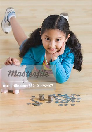 Portrait d'une jeune fille allongée sur le sol et mettre les pièces de monnaie dans une tirelire