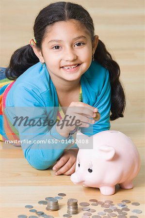 Portrait of a girl lying on the floor and putting coins into a piggy bank