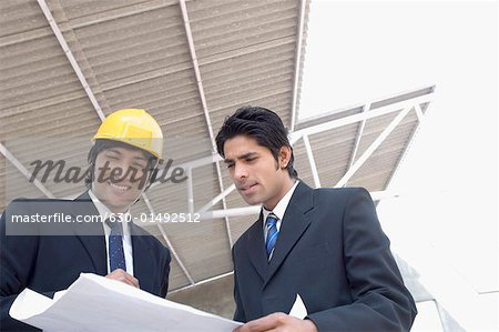 Zwei Architekten diskutieren eine Blaupause auf einer Baustelle
