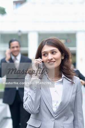 Geschäftsfrau Gespräch auf ein Mobiltelefon mit einem Geschäftsmann im Hintergrund