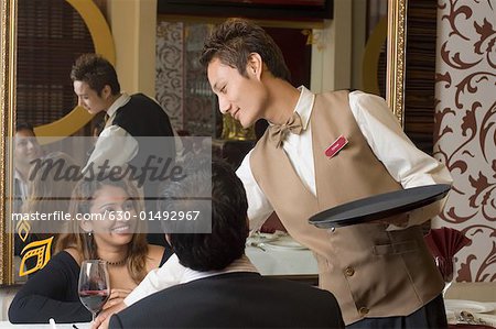 Close-up of a waiter serving wine to a young couple