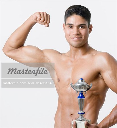 Portrait d'un jeune homme tenant un trophée et flexion ses biceps