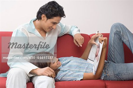 Side profile of a young couple on a couch and looking at a magazine