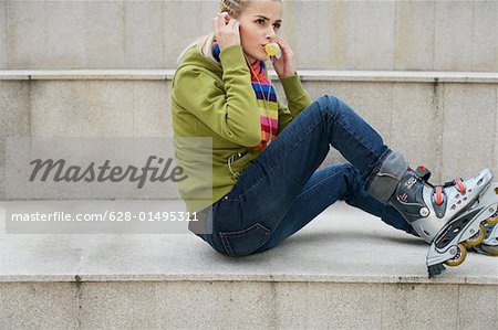 Young woman wearing inline skates listening to music about earphones sitting on staircase