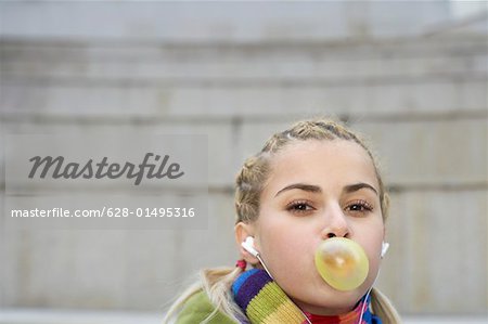 Young woman listening to music about earphones chewing gum