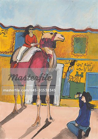 Young woman photographing her companion on a decorated camel with hieroglyphics on wall in the background
