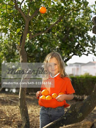 Portrait of young girl (5-7) holding oranges in front of tree, Alicante, Spain,