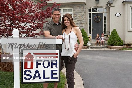 Portrait of Couple by House with For Sale Sign