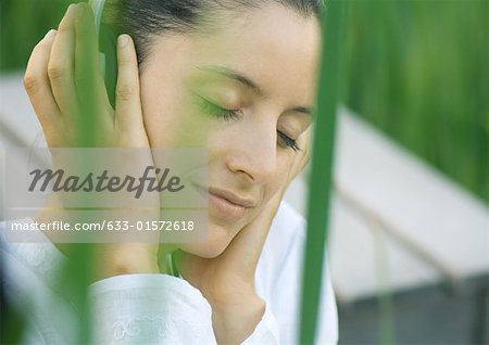 Woman listening to headphones, eyes closed, hands over ears