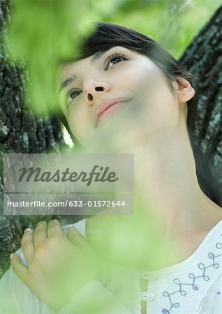 Woman with head against tree trunk, looking up