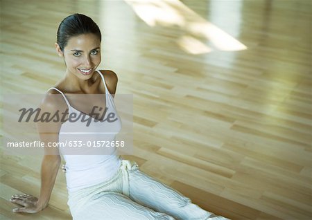 Femme assise sur le plancher d'exercice studio, souriant à la caméra