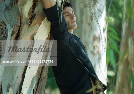 Man leaning against tree trunk, eyes closed