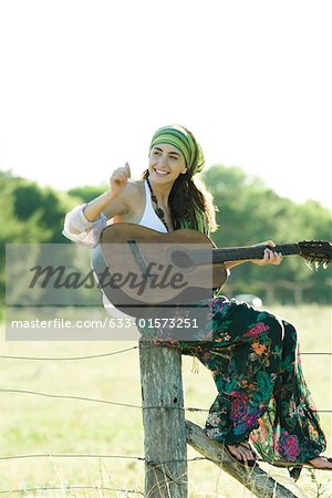 Femme jeune hippie assis sur le poteau de clôture, jouer de la guitare