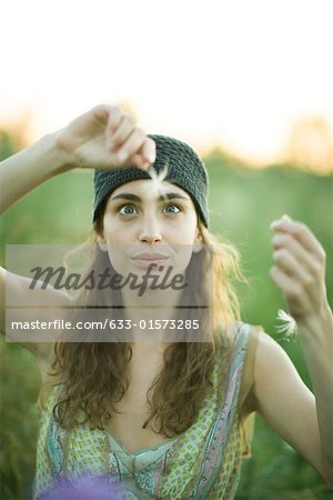 Jeune femme brandissant des tiges porte-graines de pissenlit, traversant les yeux