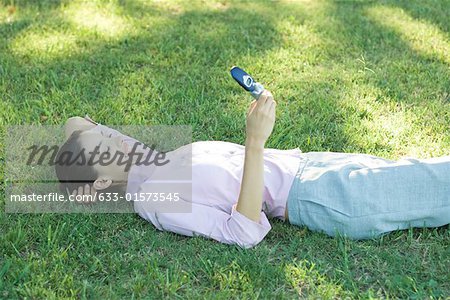 Businesswoman lying in grass, looking at cell phone, smiling