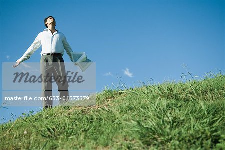 Homme debout sur la colline herbeuse, bras tendus, la tête en arrière et les yeux fermés, faible angle vue