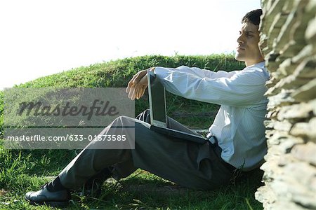 Businessman sitting on ground, holding laZSop, looking away